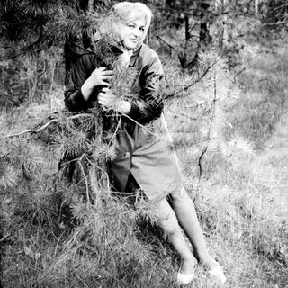 Woman seated outdoors, holding pine needles, in a grassy area.