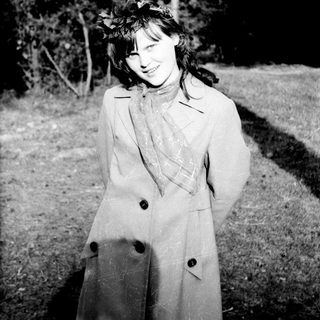 Woman in coat and flower crown smiles outdoors.