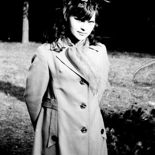 Young woman in a coat stands outdoors in a monochrome scene.