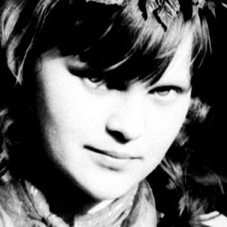 Young woman in a coat stands outdoors in a monochrome scene.