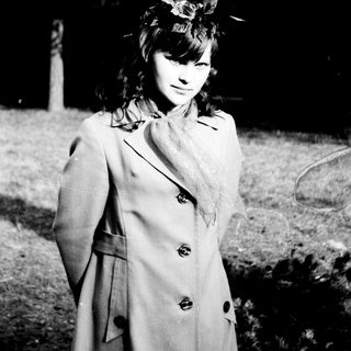 Young woman in a coat stands outdoors in a monochrome scene.