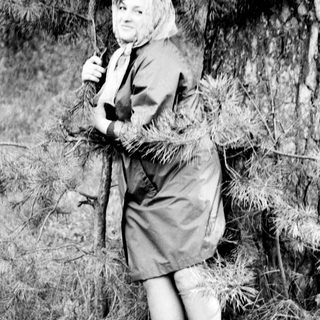 Woman in a dress leans against a pine tree.