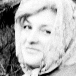 Woman in a dress leans against a pine tree.