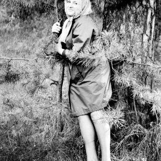 Woman in a dress leans against a pine tree.