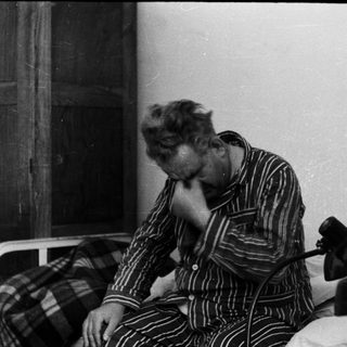Man in pajamas sits on bed, appearing distressed.