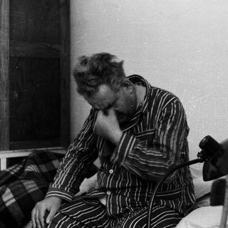Man in pajamas sits on bed, appearing distressed.