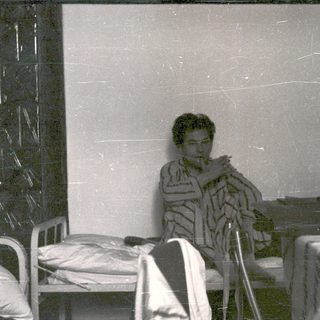 Man in robe seated, appearing to smoke indoors.