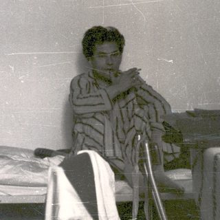 Man in robe seated, appearing to smoke indoors.