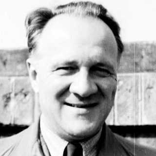 Man in a trench coat smiles for a portrait.