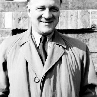 Man in a trench coat smiles for a portrait.
