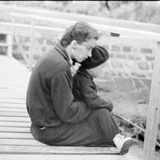 Man sits pensively on a wooden structure outdoors.