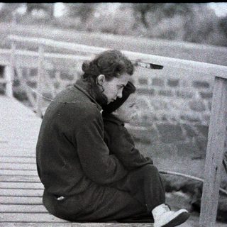 Person sits pensively on a wooden structure, looking down.