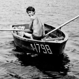 Boy rows a small boat on a lake.
