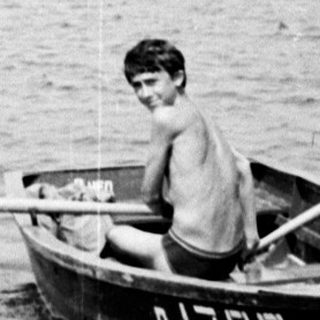 Boy rows a small boat on a lake.