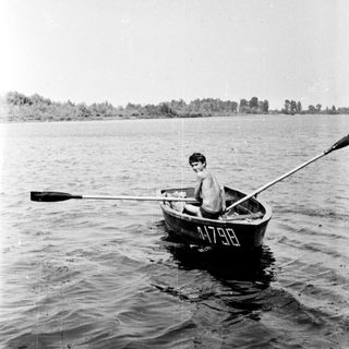 Boy rows a small boat on a lake.