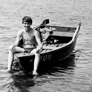 Two boys sit in a small boat on water.