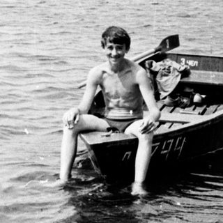 Two boys sit in a small boat on water.