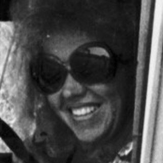 Woman in vintage vehicle, driving outdoors in a grassy area.