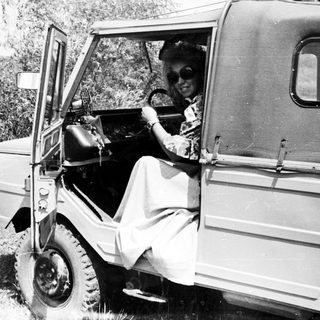 Woman driving a vintage vehicle in a grassy landscape.