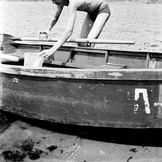 Boy in swimwear stands in a small boat.