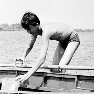 Boy in swimwear stands in a small boat.