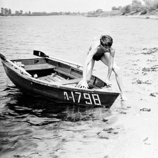 Boy exiting a small boat onto a sandy shoreline.
