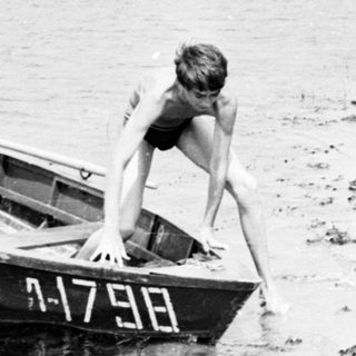 Boy exiting a small boat onto a sandy shoreline.