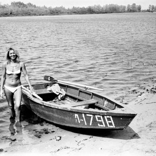 Woman stands near a boat on a sandy shoreline.