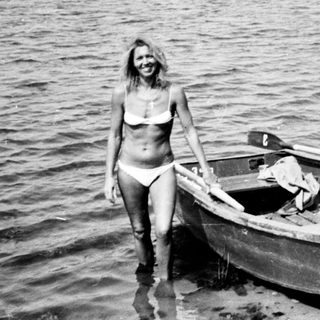Woman stands near a boat on a sandy shoreline.