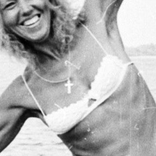 Woman in bikini standing on a boat by a lake.