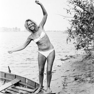 Woman in bikini standing on a boat by a lake.