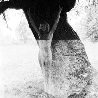 Woman stands beneath a tree with arms raised.