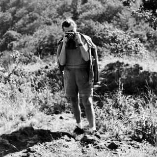 Man with camera hikes on a hillside path.