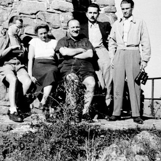 Four men and a woman posing near a stone wall.