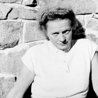 Here's a brief summary of the image: Woman standing near a stone wall, looking toward the camera.
