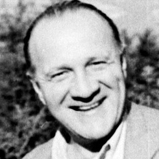 Man smiles, posed with foliage and a distant landscape.