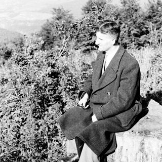 Man seated outdoors, overlooking a landscape with vegetation.