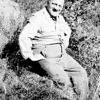 Man sitting outdoors, smiling, surrounded by vegetation.