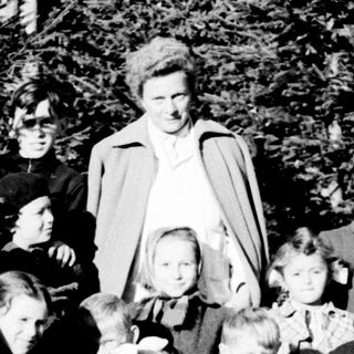 Group of children and an adult standing near trees.