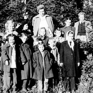 Group of children and an adult standing near trees.