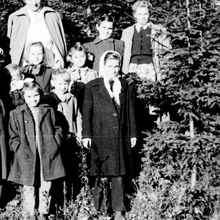 Group of children and an adult standing near trees.