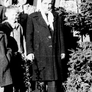 Group of children and an adult stand in a wooded area.