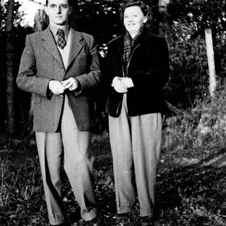 A couple poses outdoors in a wooded area.