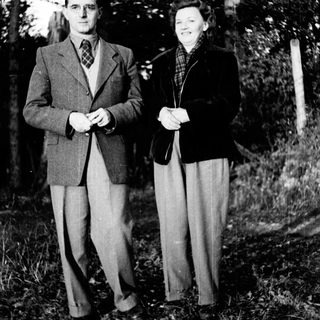 A couple poses outdoors in a wooded area.