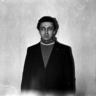Man in suit stands facing camera in a room.