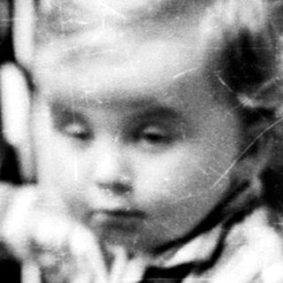 Here's a brief summary of the image: A young child stands near a staircase, looking downward.