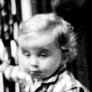 Here's a brief summary of the image: A young child stands near a staircase, looking downward.