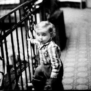 Here's a brief summary of the image: A young child stands near a staircase, looking downward.