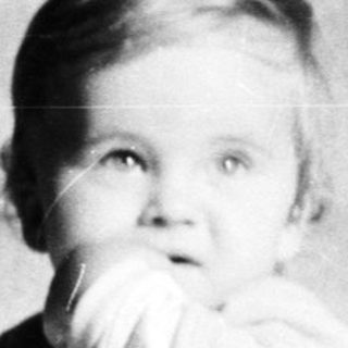 Baby peering over a crib railing in a vintage photograph.