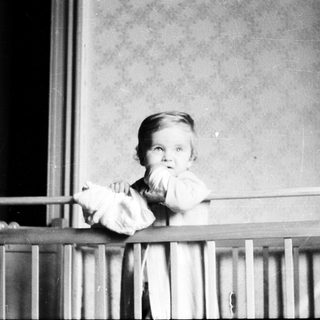 Baby peering over a crib railing in a vintage photograph.